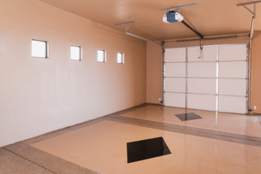Interior of an empty garage with tan walls, a tiled floor and a white sectional door with ceiling-mounted opener