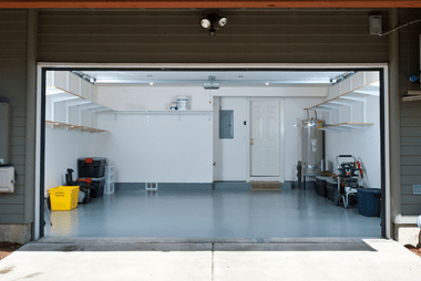 Interior view looking out through an open garage door into a two-car garage with shelving and stored items