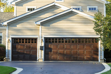 Two dark wood carriage-style garage doors on a beige house
