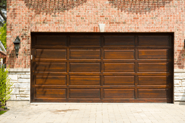 Dark wood-panel garage door on a brick house flanked by wall lanterns
