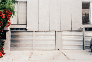 Row of grey roller doors on a building facade with red flowering bougainvillea in front