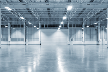Interior of an empty industrial warehouse with steel roller doors and a polished reflective floor