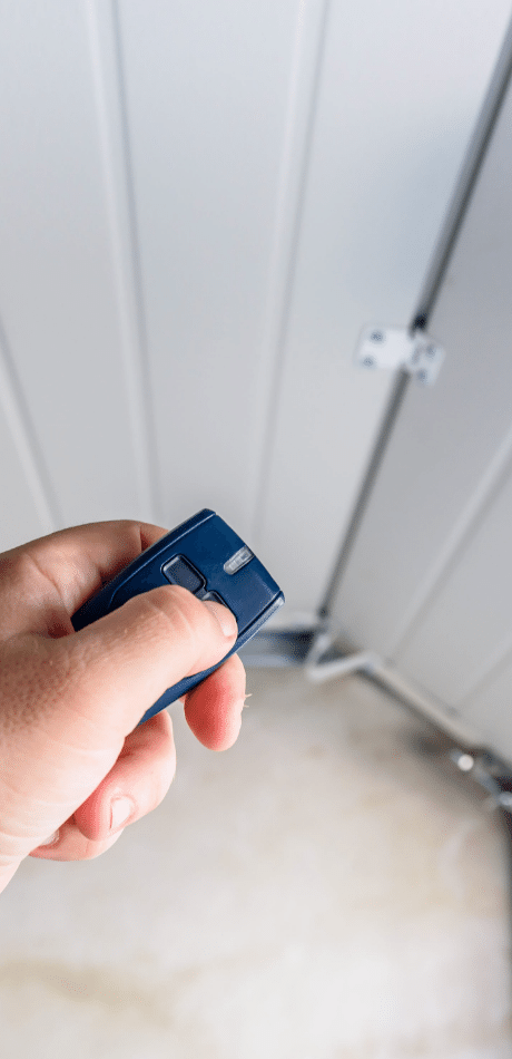 Hand holding a remote control beside a white sectional garage door track