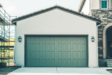 Sage green sectional garage door on a light-coloured stucco house with wall lanterns