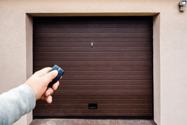 Hand pointing a remote control at a closed dark brown roller door