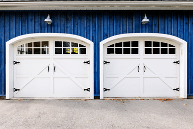 Two white carriage-style garage doors with arched windows on a dark blue-painted building