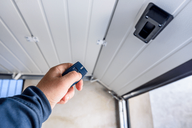 Hand pointing a remote control at a garage door opener sensor