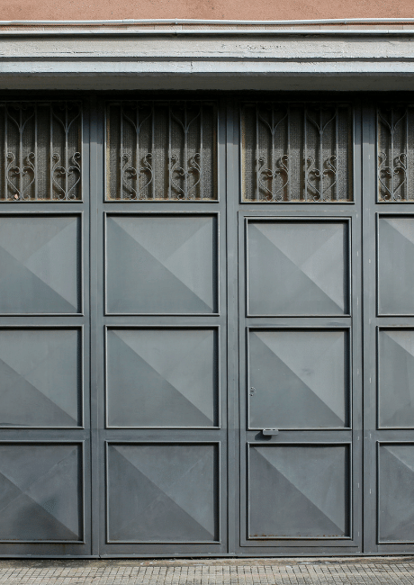 Grey metal panelled double garage door with decorative wrought-iron style transom grilles