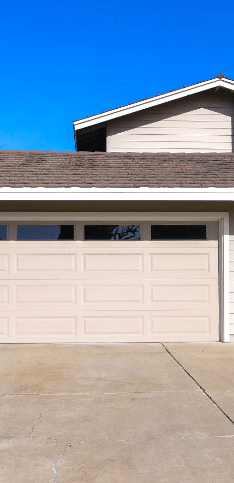 Off-white sectional garage door with tinted upper windows on a house, viewed from the driveway