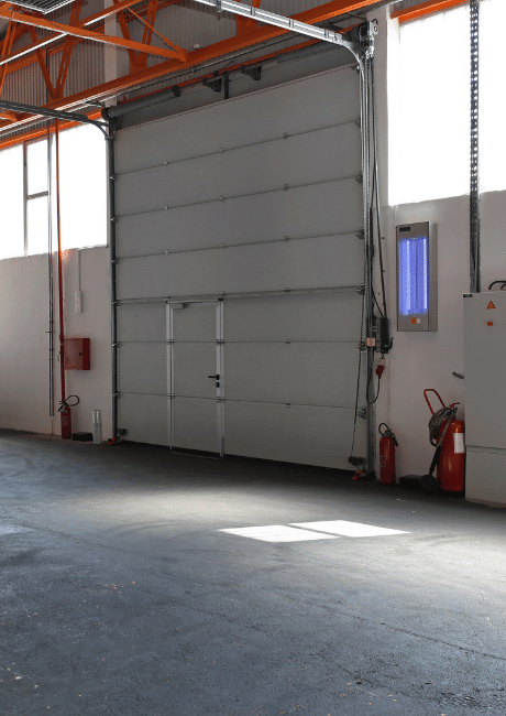 Interior of a commercial building with a large light grey sectional door partially raised and fire extinguishers nearby