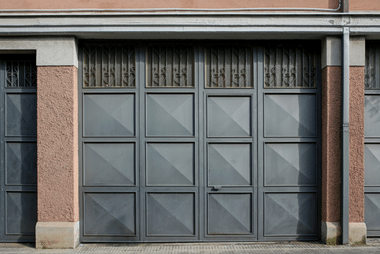 Grey panelled double garage door with decorative grille transoms flanked by brick and stucco pillars