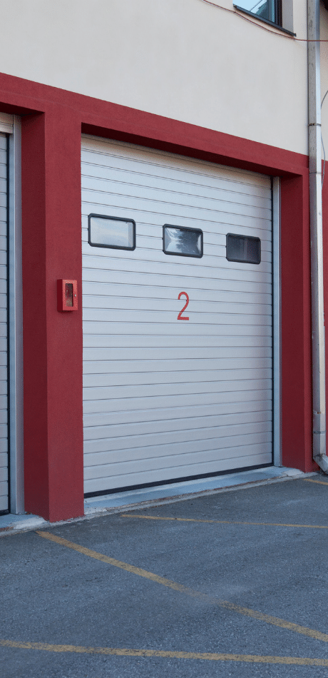 White roller door with a number 2 in red on a red-painted door surround, in a car park