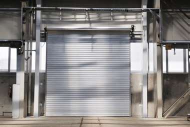 White roller door raised partway inside a steel-framed industrial warehouse loading bay.