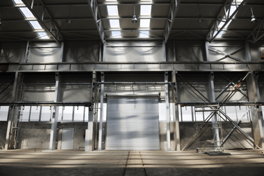 Interior of a steel-framed warehouse with a closed white roller door built into the loading bay wall.