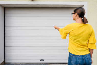 Woman in a yellow top pointing a garage door remote at a white roller door
