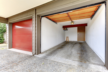 Two adjoining garages, one with a closed red roller door and the other open, revealing an empty concrete-floored bay.
