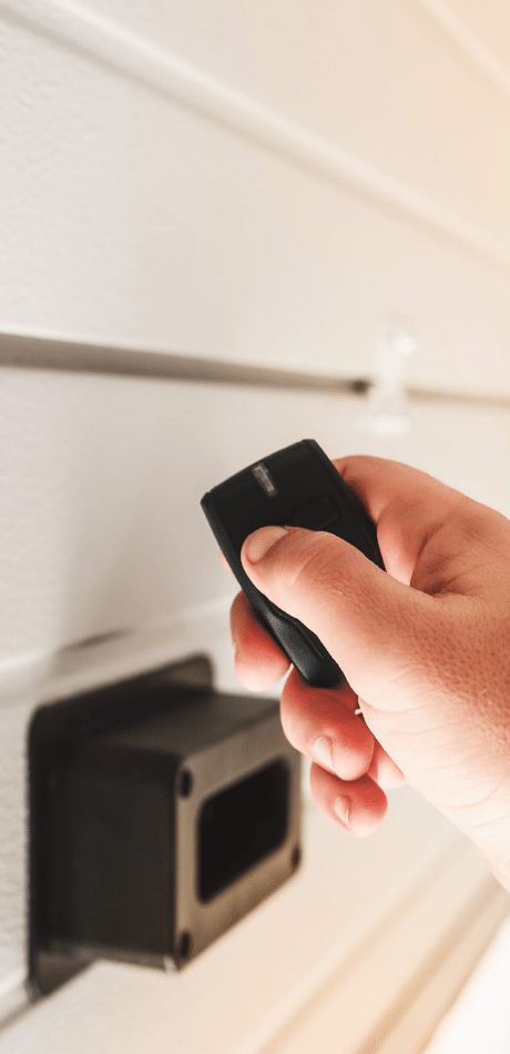 Hand holding a remote control near a black garage door sensor unit