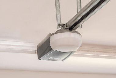 Close-up of a garage door opener motor mounted on the ceiling rail near the top of the door frame.