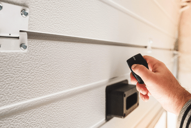 Hand pointing a remote control at a white roller door beside its motor unit