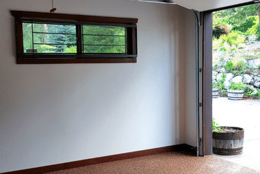 Interior of a home garage looking toward the open door, with a small window and a view of the garden outside.