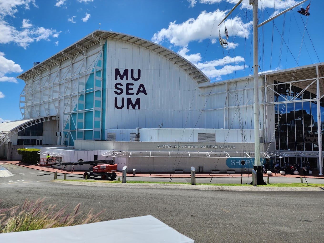 White curved-roof museum building with 'MUSEUM' lettering on its facade and ship masts and rigging in front.