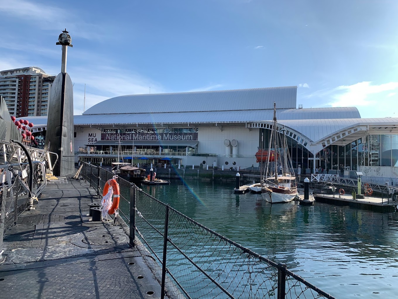 View along the deck of a docked submarine toward the museum building and a marina with moored boats.